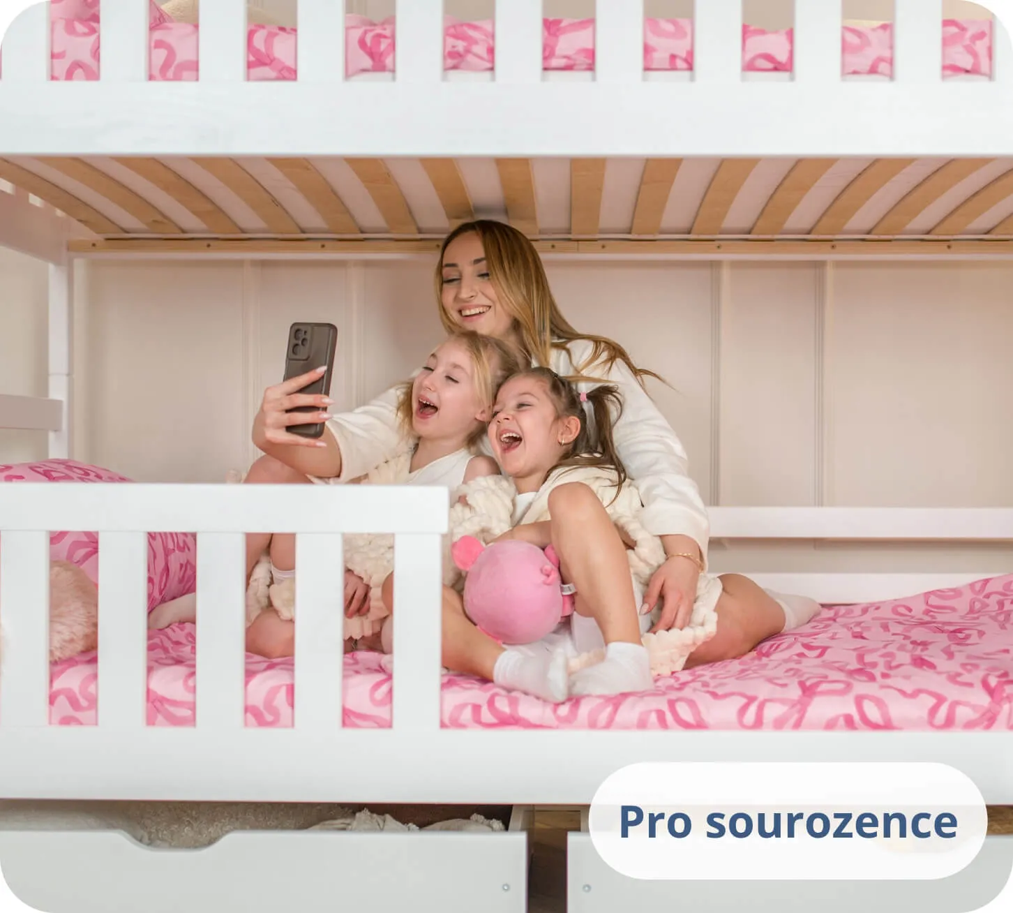 Dvě dívky a žena smějící se do telefonu na bílé palandě.